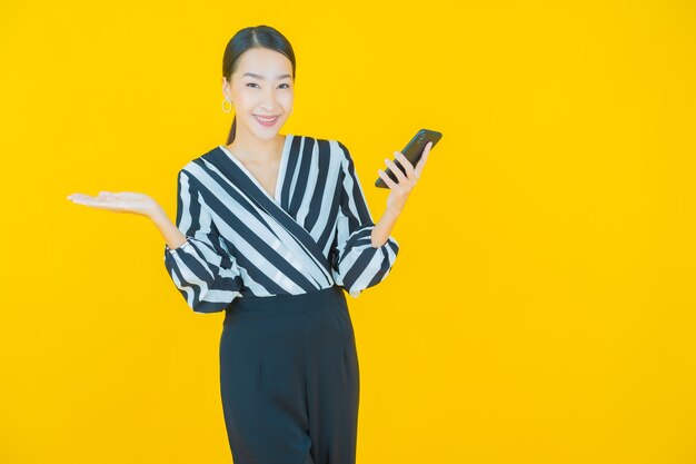 黄色のスマート携帯電話で笑顔美しい若いアジアの女性の肖像画