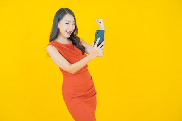 노란색에 스마트 휴대 전화와 함께 초상화 아름 다운 젊은 아시아 여자 미소