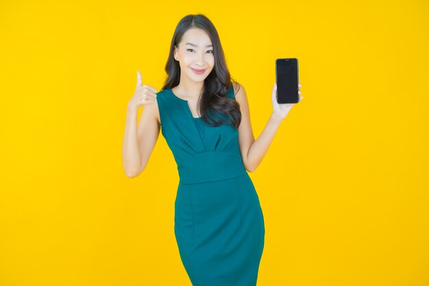 黄色のスマート携帯電話で笑顔美しい若いアジアの女性の肖像画