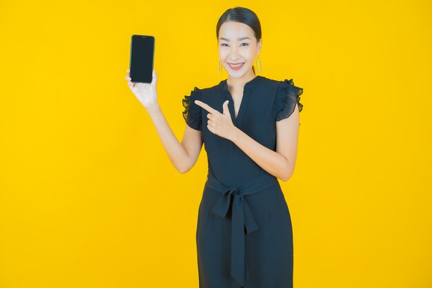 黄色の上のスマートな携帯電話で笑顔美しい若いアジアの女性の肖像画