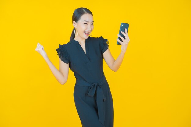 黄色の上のスマートな携帯電話で笑顔美しい若いアジアの女性の肖像画