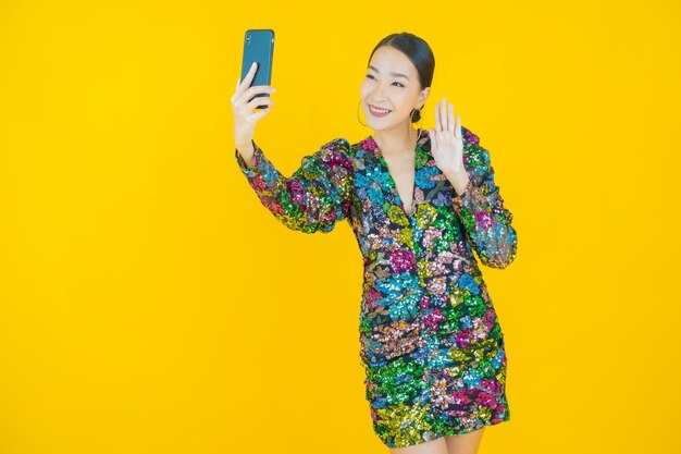 黄色のスマート携帯電話で笑顔美しい若いアジアの女性の肖像画