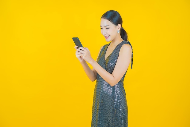 노란색에 스마트 휴대 전화와 함께 초상화 아름 다운 젊은 아시아 여자 미소