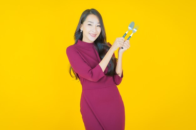 노란색에 숟가락과 포크로 웃는 아름다운 젊은 아시아 여성 초상화