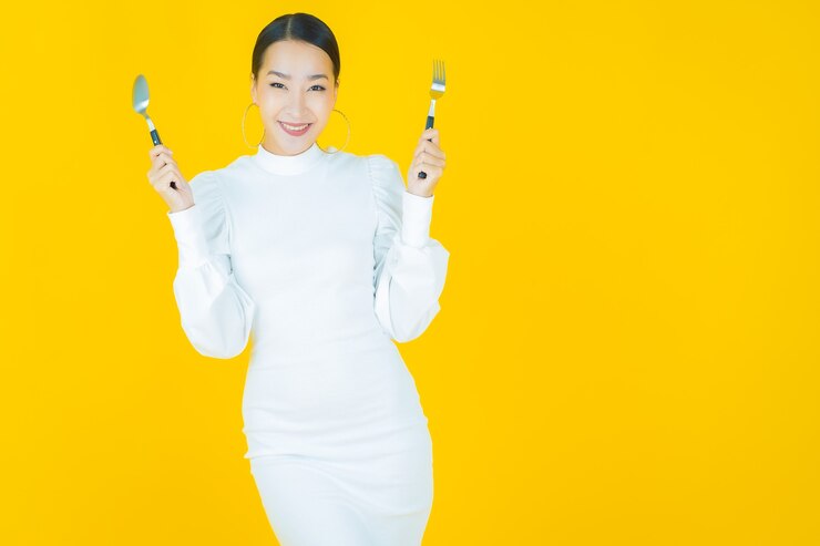 無料Photo 黄色のスプーンとフォークで笑顔美しい若いアジアの女性の肖像画