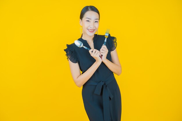 Portrait beautiful young asian woman smile with spoon and fork on on yellow