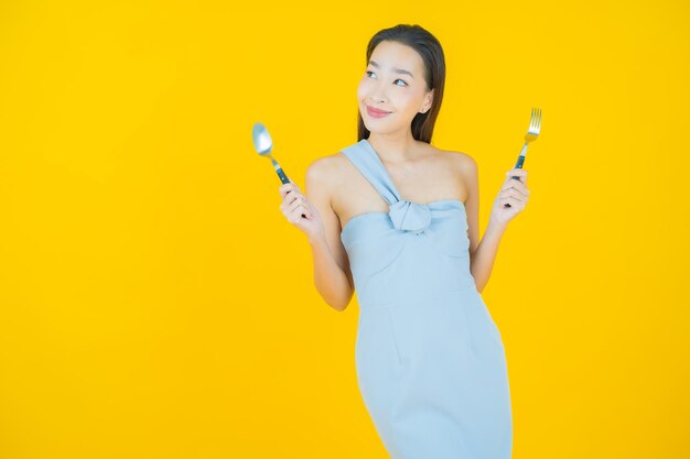 Ritratto bella giovane donna asiatica sorriso con cucchiaio e forchetta su yellow
