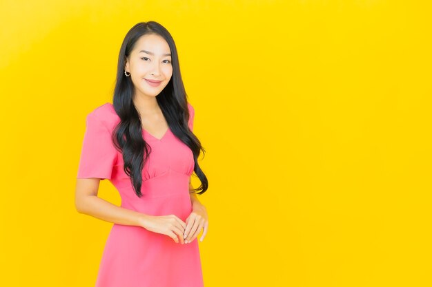 Portrait of beautiful young asian woman smiles in pink dress on yellow wall