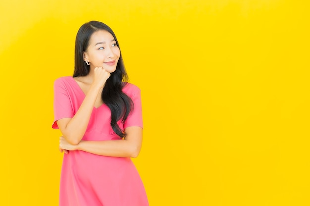 Портрет красивой молодой азиатской женщины улыбается в розовом платье на желтой стене