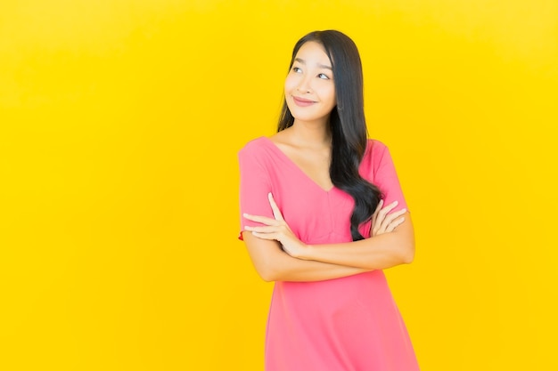 Portrait of beautiful young asian woman smiles in pink dress on yellow wall
