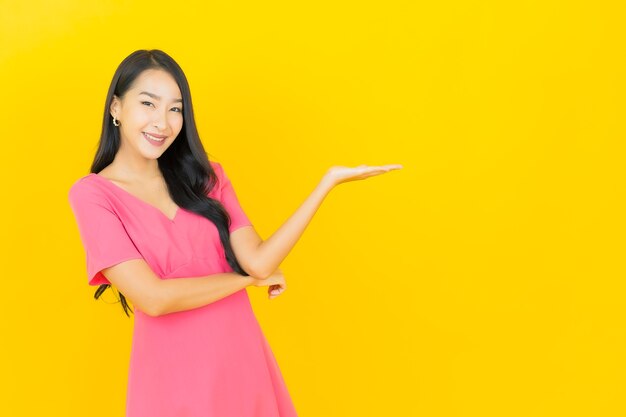 Portrait of beautiful young asian woman smiles in pink dress on yellow wall