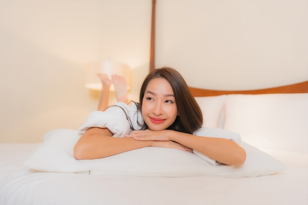 肖像画美しい若いアジアの女性の笑顔が寝室のインテリアのベッドでリラックス