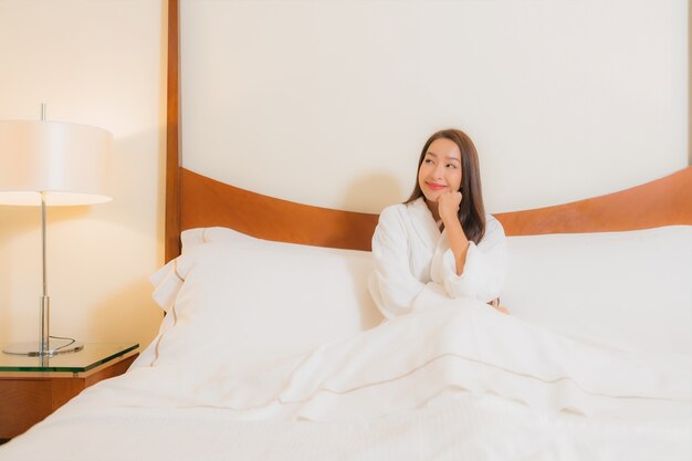 Улыбка женщины портрета красивая молодая азиатская ослабляя на кровати в интерьере спальни