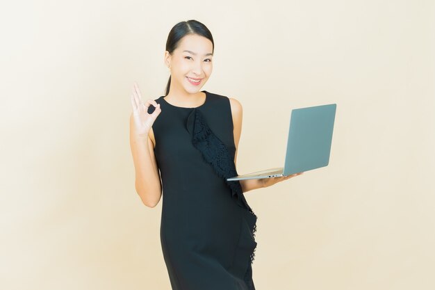 Portrait beautiful young asian woman smiles with computer laptop on isolated wall