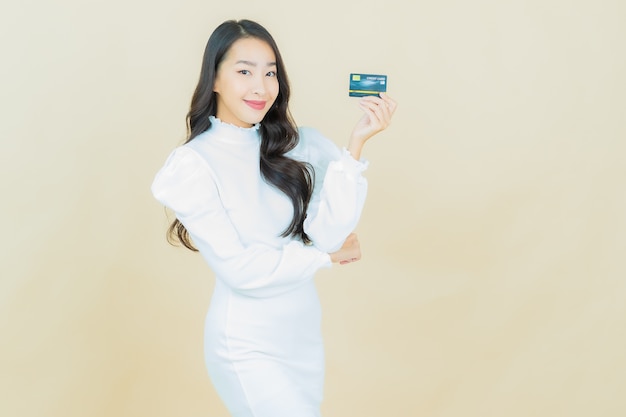 Портрет красивой молодой азиатской женщины улыбается с кредитной картой на стене цвета