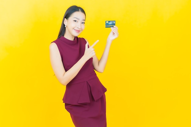 Улыбка женщины портрета красивая молодая азиатская с кредитной картой на желтой стене