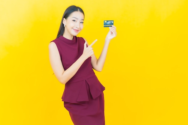 Portrait beautiful young asian woman smiles with credit card on yellow wall