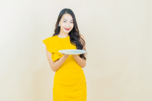 베이지색 벽에 빈 접시 접시를 들고 웃는 아름다운 젊은 아시아 여성