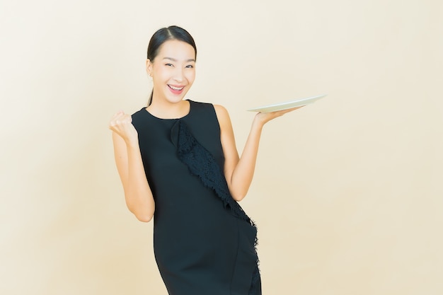 Portrait beautiful young asian woman smiles with empty plate dish on color wall