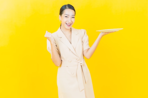 Portrait beautiful young asian woman smiles with empty plate dish on color wall