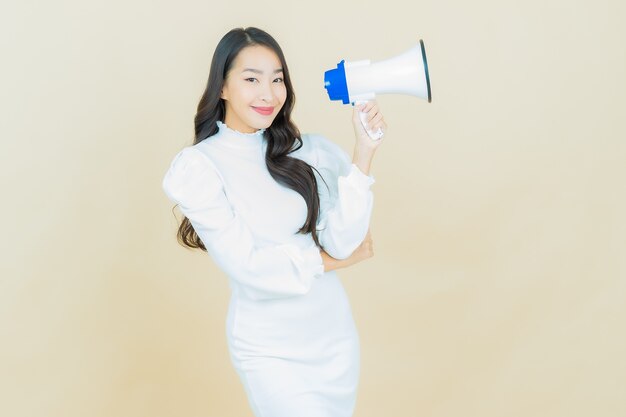 Портрет красивой молодой азиатской женщины улыбается с мегафоном на стене цвета