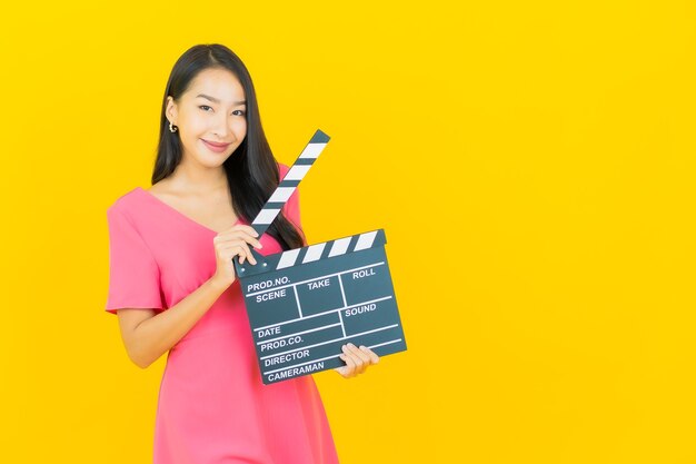 Portrait beautiful young asian woman smiles with movie slate plate cutting on yellow wall