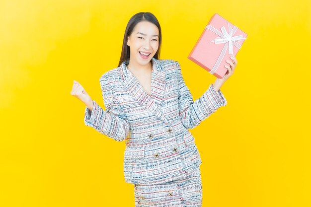 Portrait beautiful young asian woman smiles with red gift box on color wall