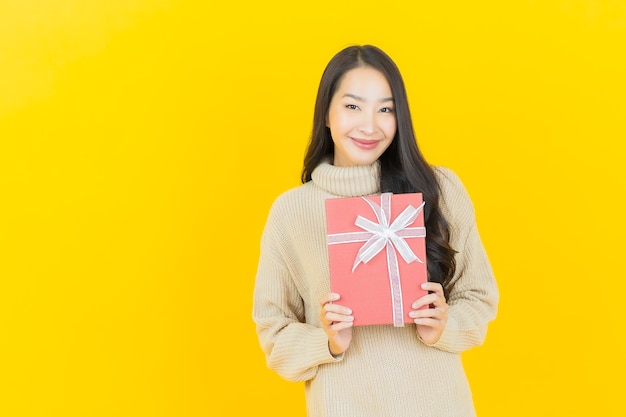 Portrait beautiful young asian woman smiles with red gift box on yellow wall