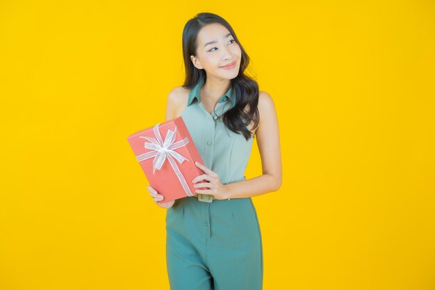 Portrait of beautiful young asian woman smiles with red gift box on yellow wall