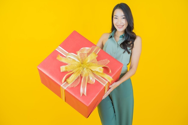 Portrait of beautiful young asian woman smiles with red gift box on yellow wall