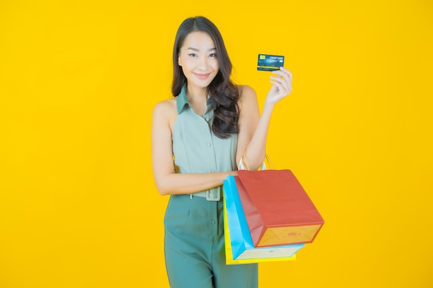 Portrait of beautiful young asian woman smiles with shopping bag on yellow wall