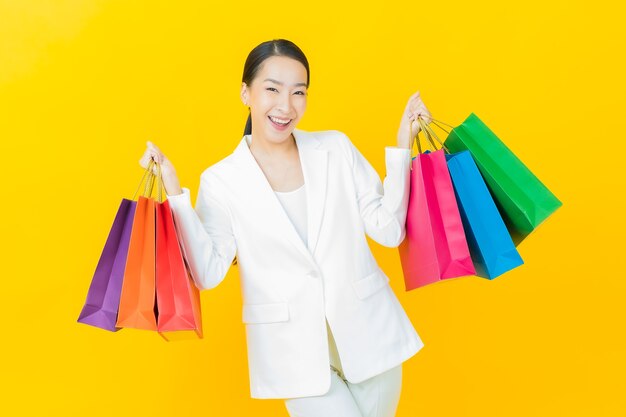 Portrait beautiful young asian woman smiles with shopping bags on color wall