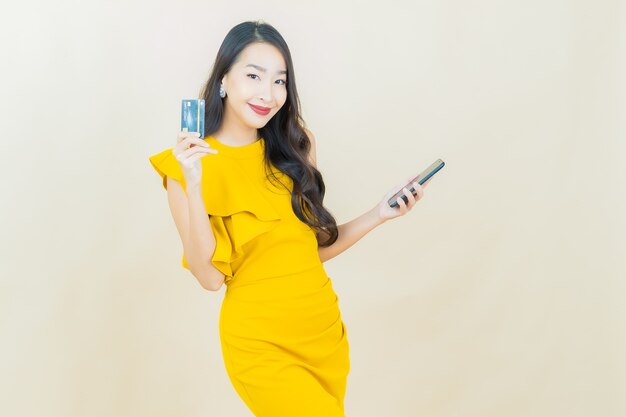 Улыбка женщины портрета красивая молодая азиатская с умным мобильным телефоном на бежевой стене