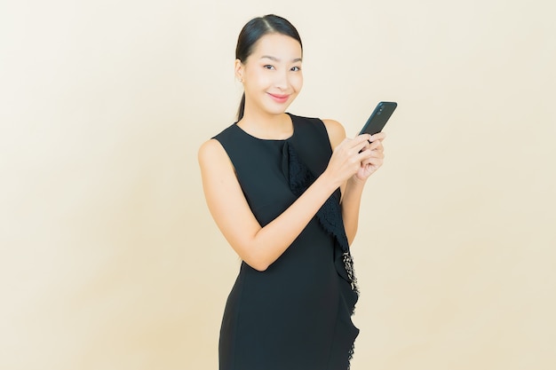 Portrait beautiful young asian woman smiles with smart mobile phone on color wall