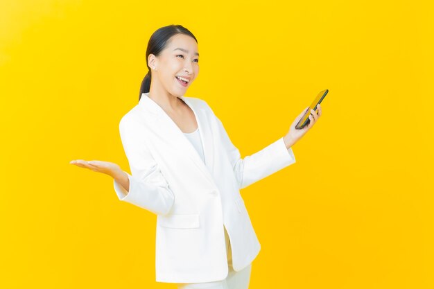아름다운 젊은 아시아 여성이 컬러 벽에 스마트 휴대폰을 들고 미소를 짓고 있다