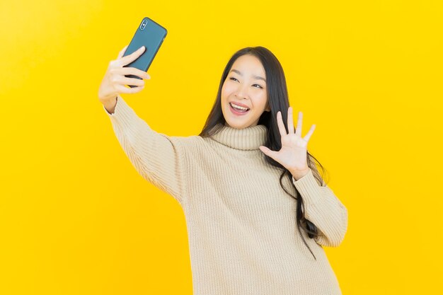 Portrait beautiful young asian woman smiles with smart mobile phone on yellow wall