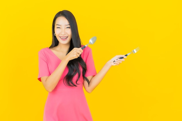 Portrait beautiful young asian woman smiles with spoon and fork on yellow wall