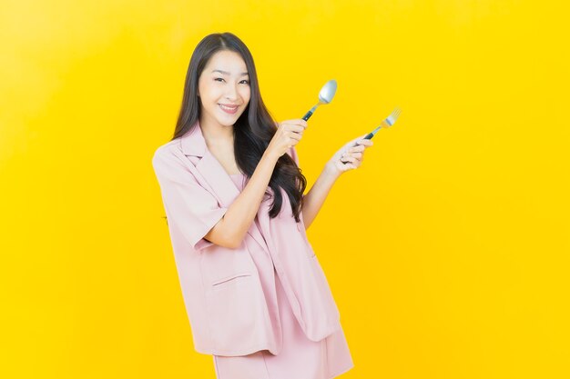 Portrait beautiful young asian woman smiles with spoon and fork on yellow wall