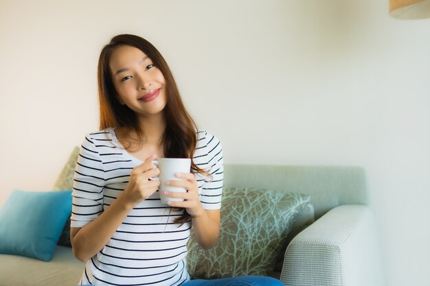 コーヒーカップが付いているソファーの肖像画美しい若いアジア女性