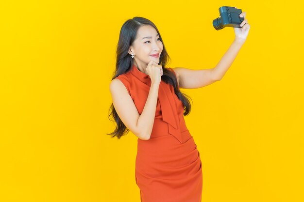 Portrait beautiful young asian woman use camera on yellow