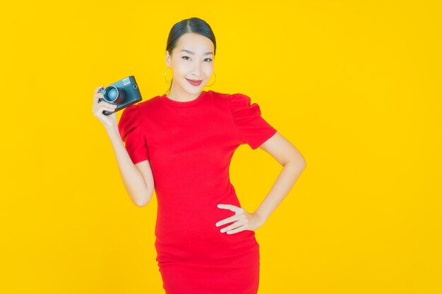 Портрет красивой молодой азиатской женщины использует камеру на желтом