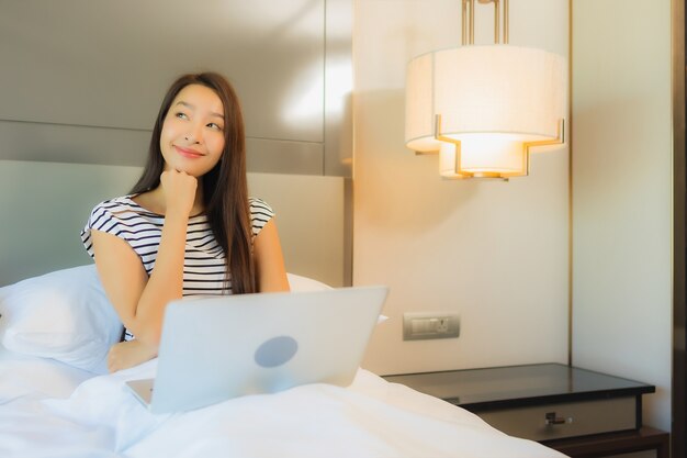 Portrait beautiful young asian woman use computer laptop on bed in bedroom interior