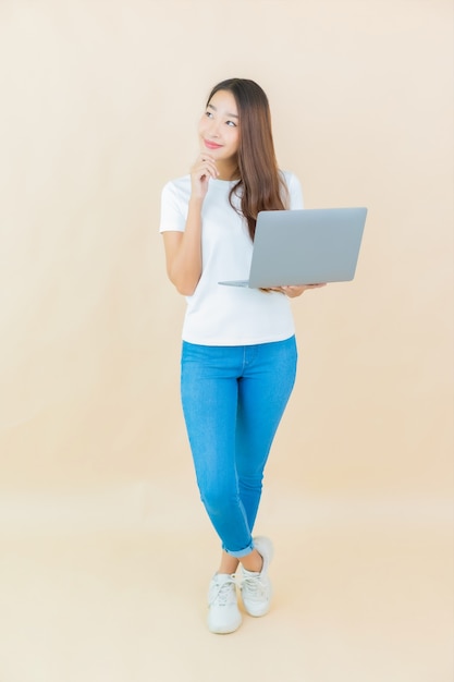 Foto gratuita computer portatile del computer di uso della bella giovane donna asiatica del ritratto sul beige