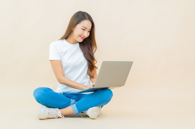 세로 아름 다운 젊은 아시아 여자 베이지 색에 컴퓨터 노트북을 사용