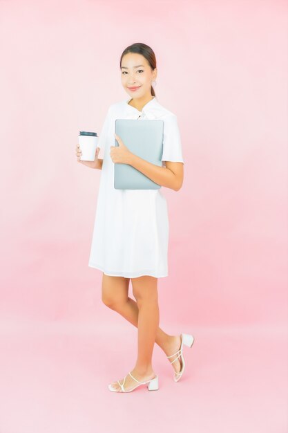 肖像画美しい若いアジアの女性はピンクの壁にコンピューターのラップトップを使用します