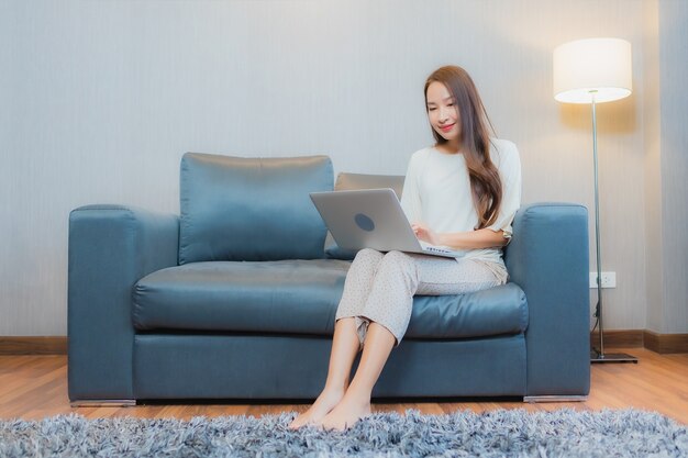 세로 아름 다운 젊은 아시아 여자 거실 인테리어에 소파에 컴퓨터 노트북을 사용