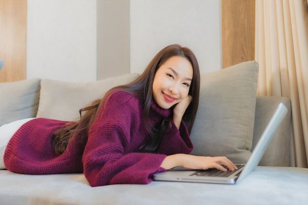 세로 아름 다운 젊은 아시아 여자 소파에 온라인 쇼핑을 위해 신용 카드로 컴퓨터 노트북을 사용