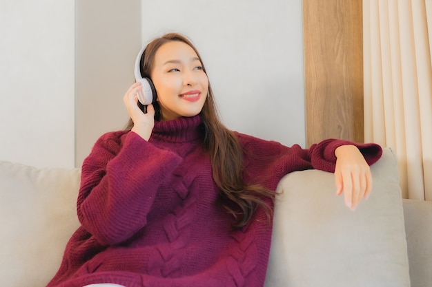 Наушники пользы женщины портрета красивые молодые азиатские для слушать музыку на софе в интерьере живущей комнаты