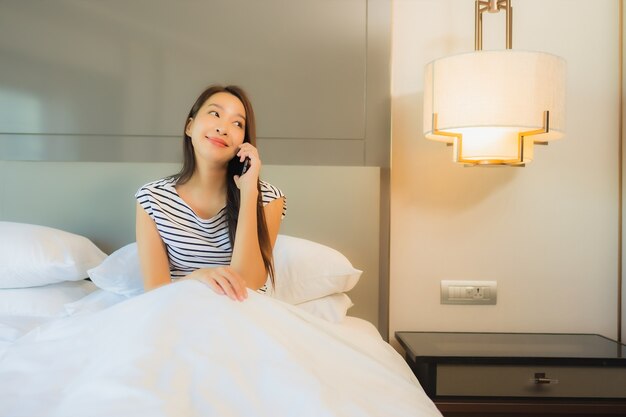 Portrait beautiful young asian woman use smart mobile phone on bed in bedroom interior