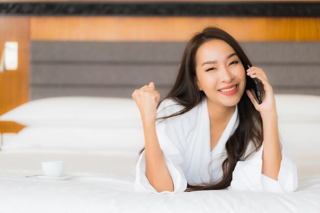 세로 아름 다운 젊은 아시아 여자 침실 인테리어에 침대에 스마트 휴대 전화를 사용